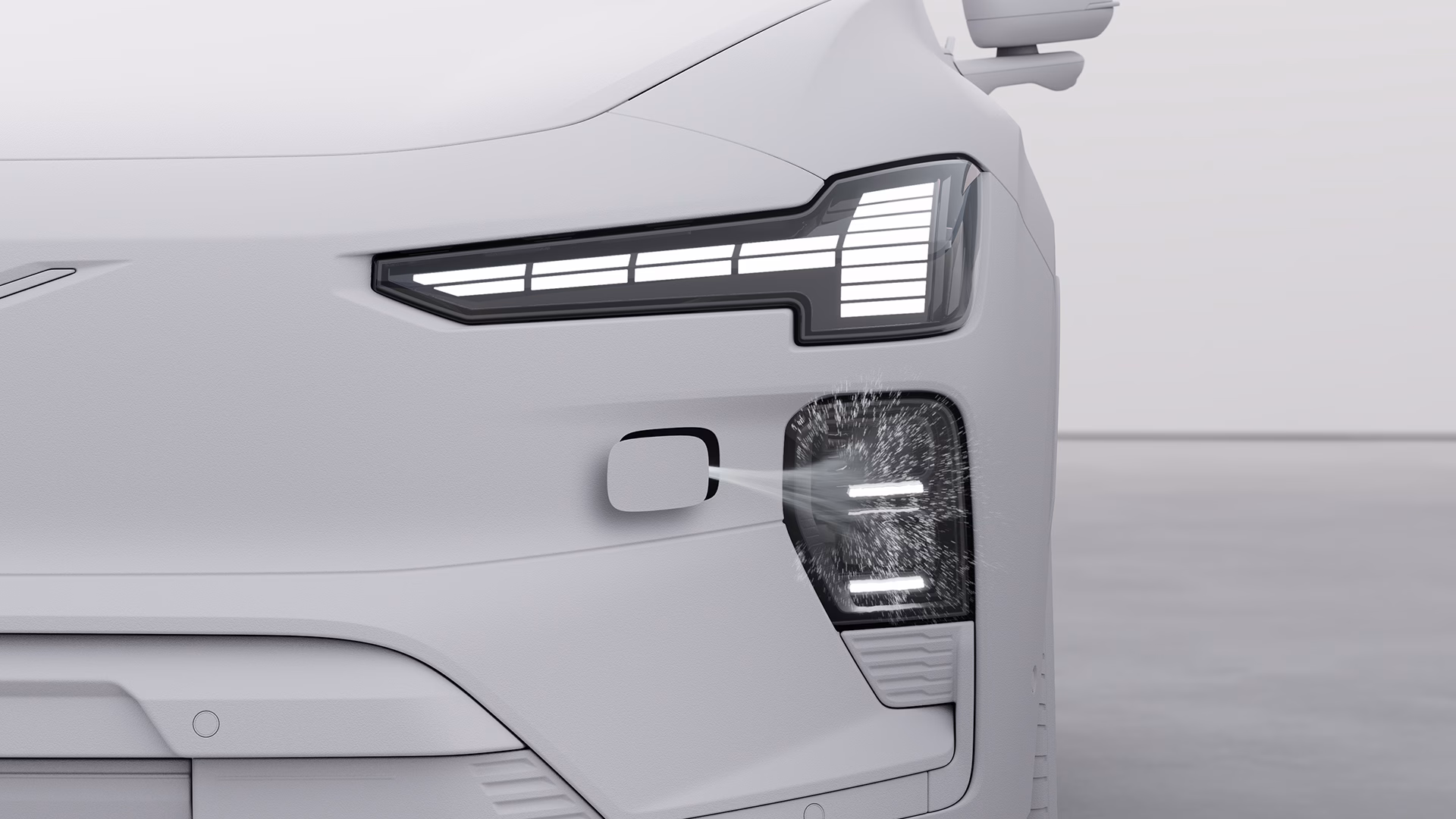 Крупный план передней фары автомобиля Volvo, на котором показана работающая система омывателей фар с распылением воды на объектив.