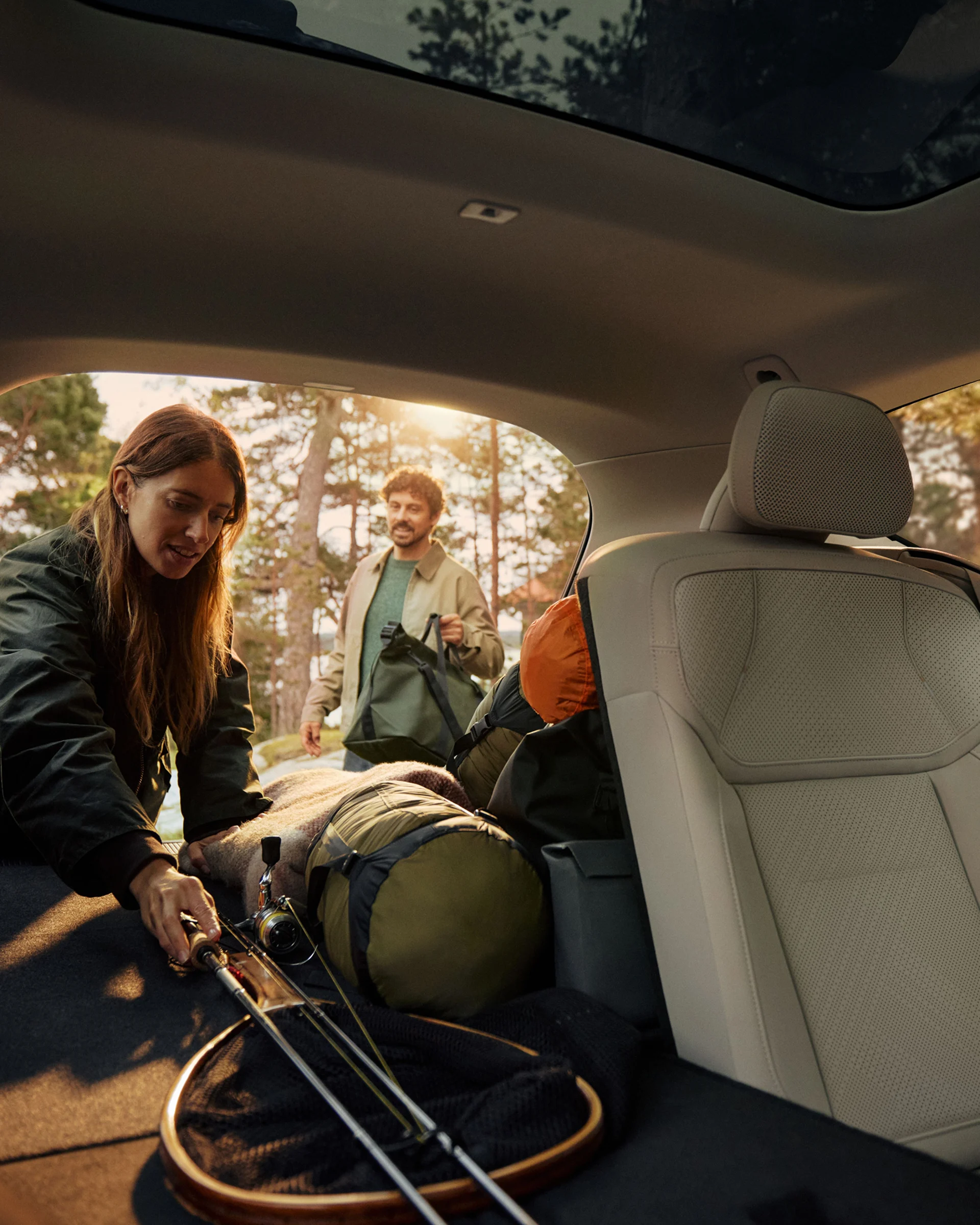 Два человека загружают снаряжение для активного отдыха в кузов Volvo EX60 со сложенными задними сиденьями.