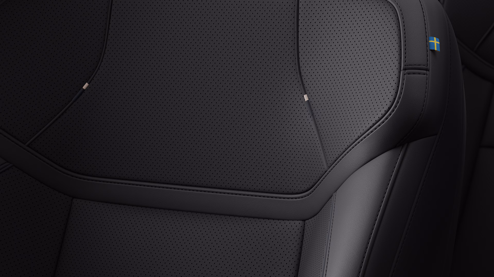 Крупный план автомобильного сиденья Volvo с черной перфорированной обивкой и небольшой биркой шведского флага сбоку.