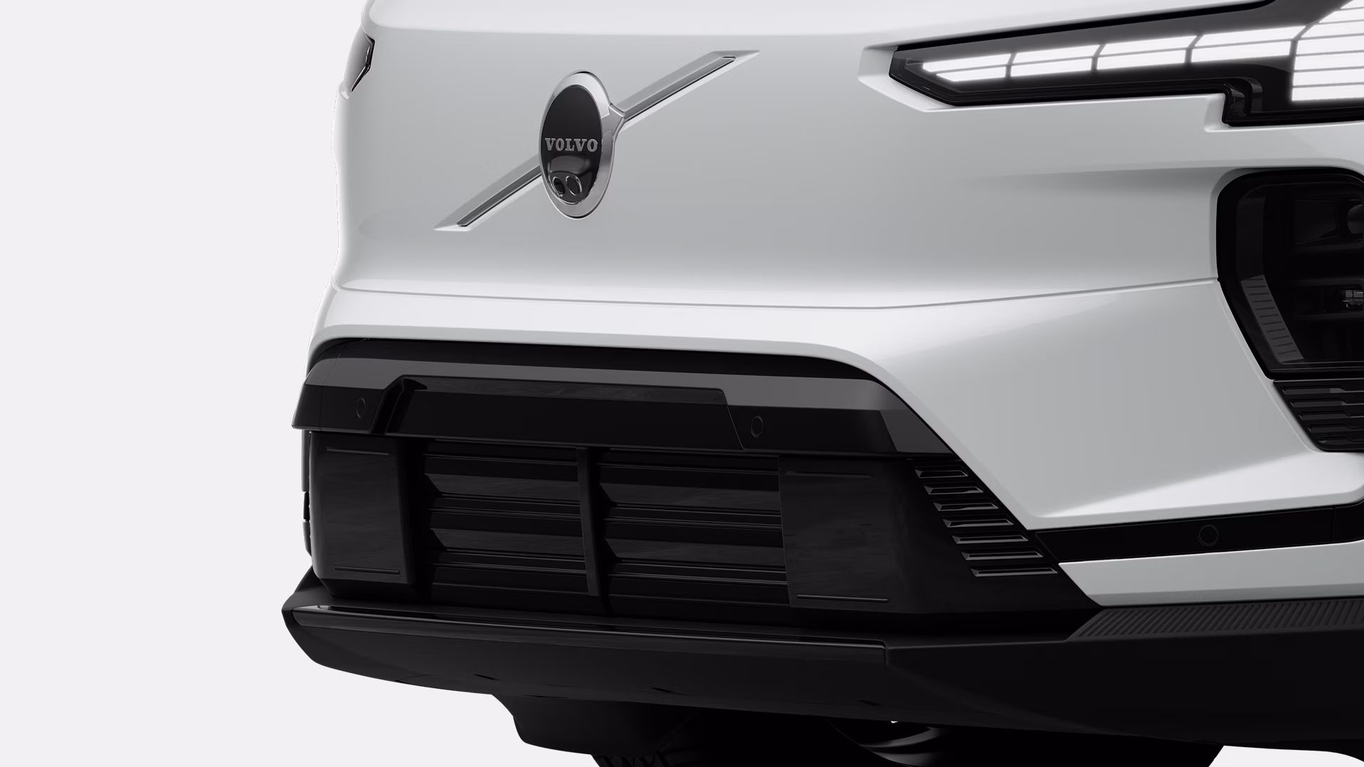 Крупный план передней решетки радиатора и фары автомобиля Volvo с логотипом Volvo и современными элементами дизайна.