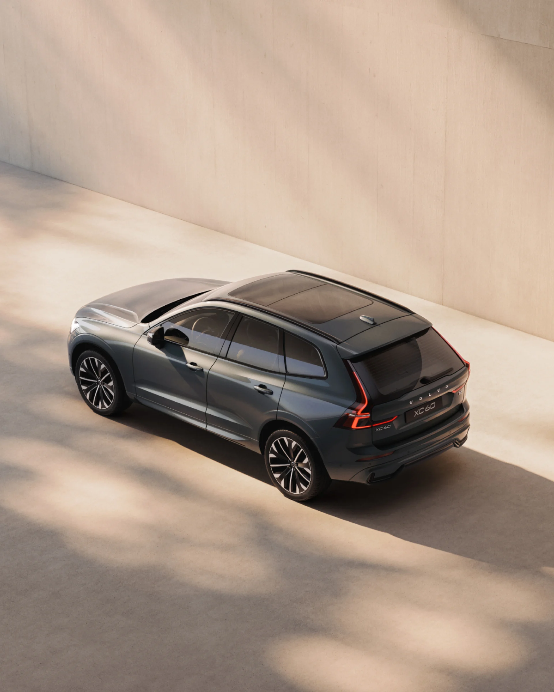 Вид сзади на среднеразмерный мягкий гибридный внедорожник Volvo XC60, с панорамной крышей и характерными светодиодными задними фонарями.