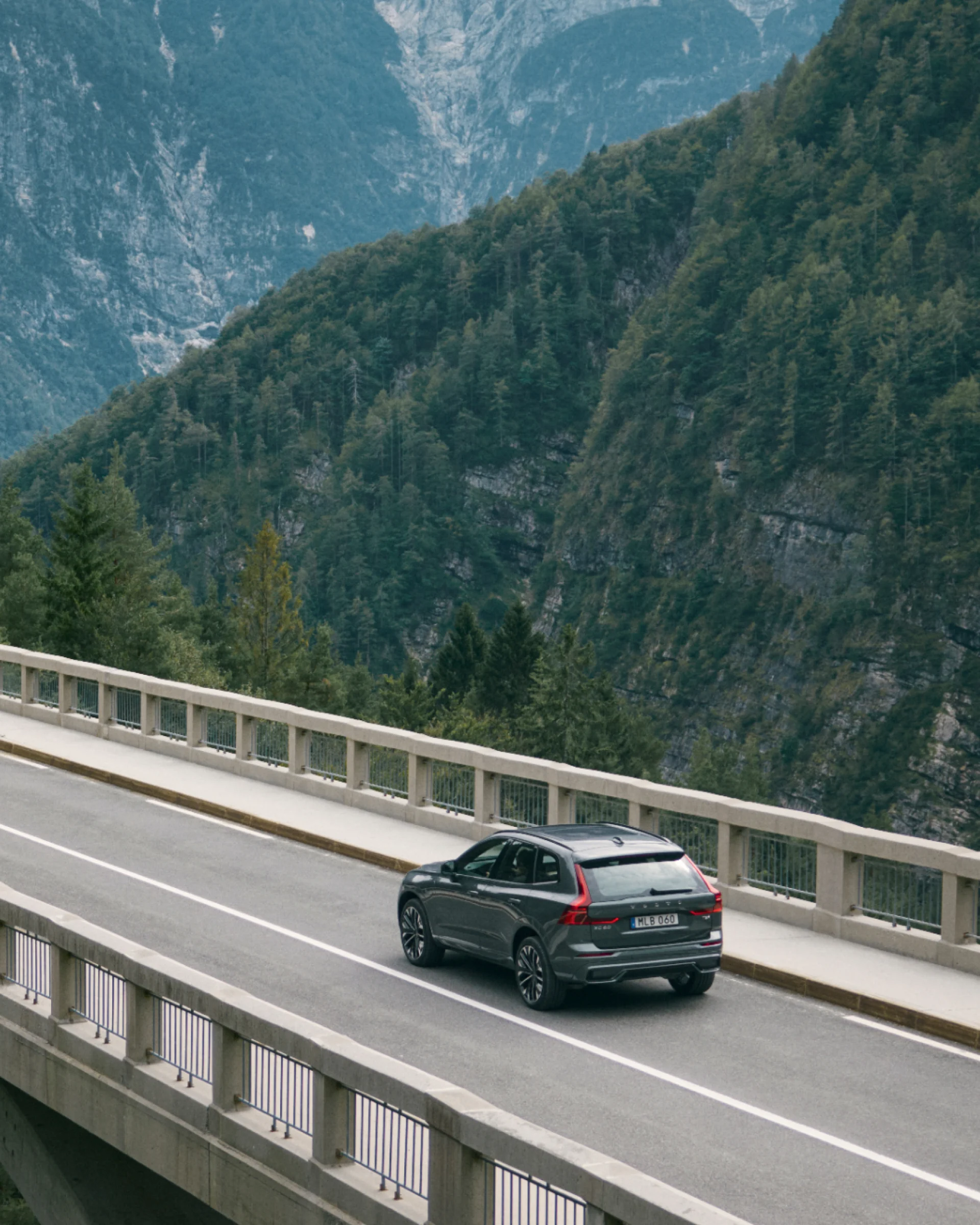 Volvo XC60 едет по мосту на фоне горного пейзажа.