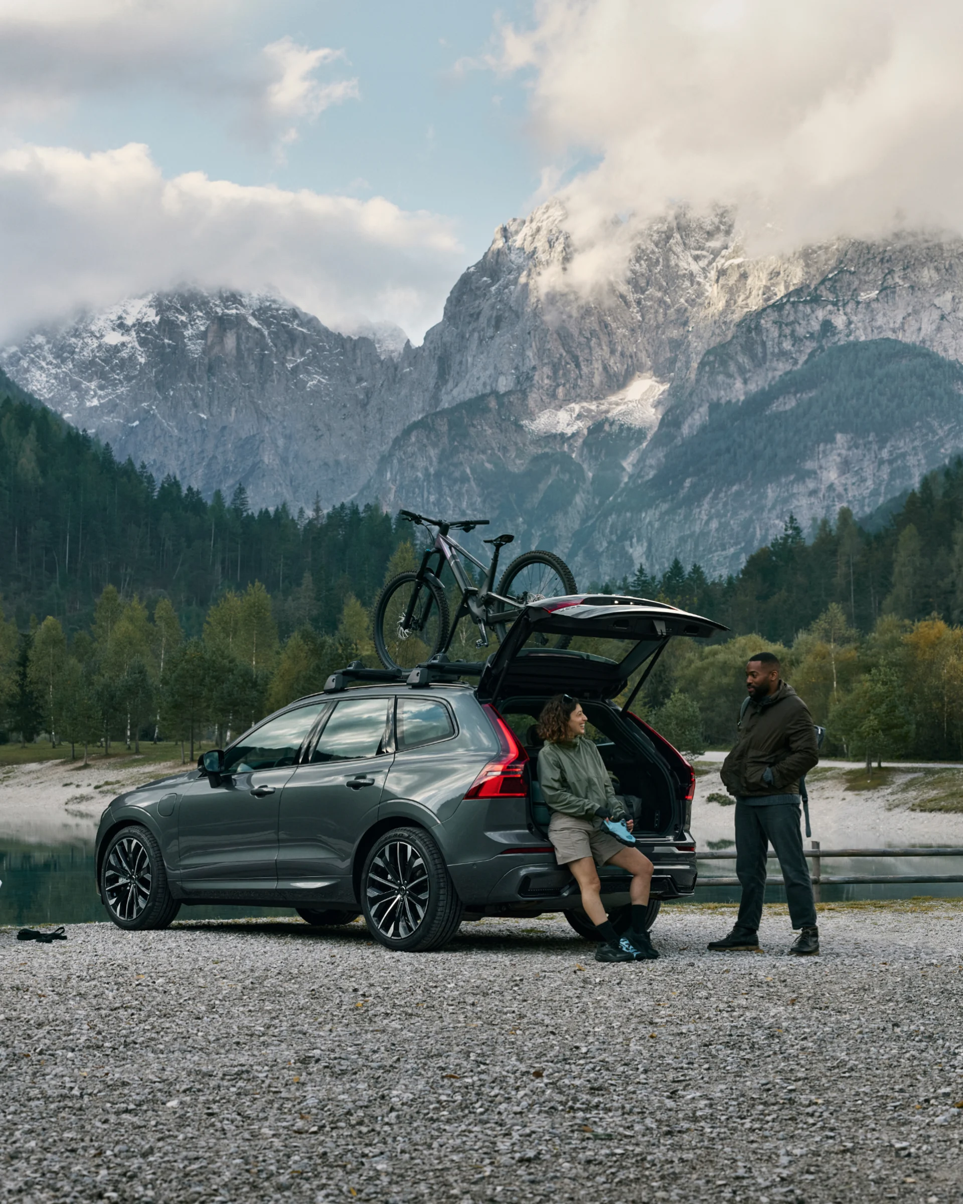 Два человека отдыхают у открытого багажника Volvo XC60, припаркованного на живописной дороге с велосипедом, прикрепленным к крыше.