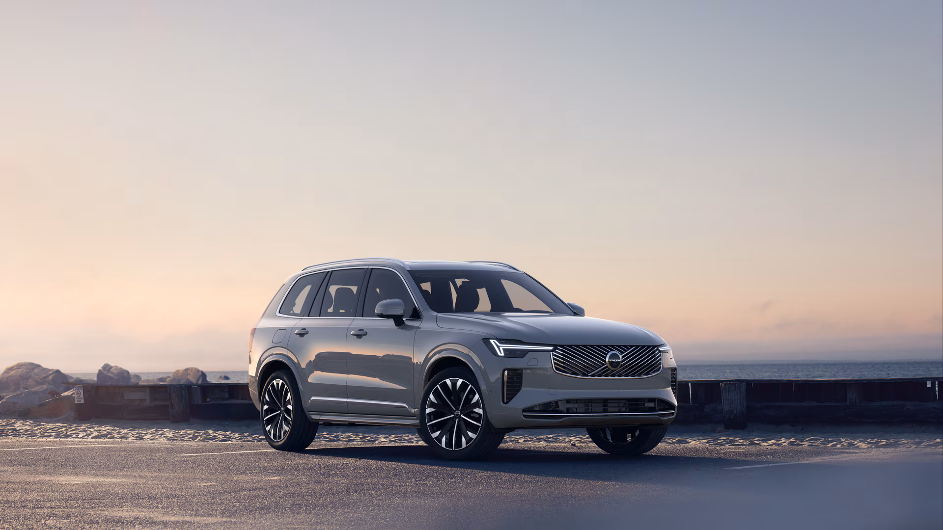 Автомобиль Volvo в три четверти на прибрежной дороге, спереди и сбоку на безмятежном фоне океана.