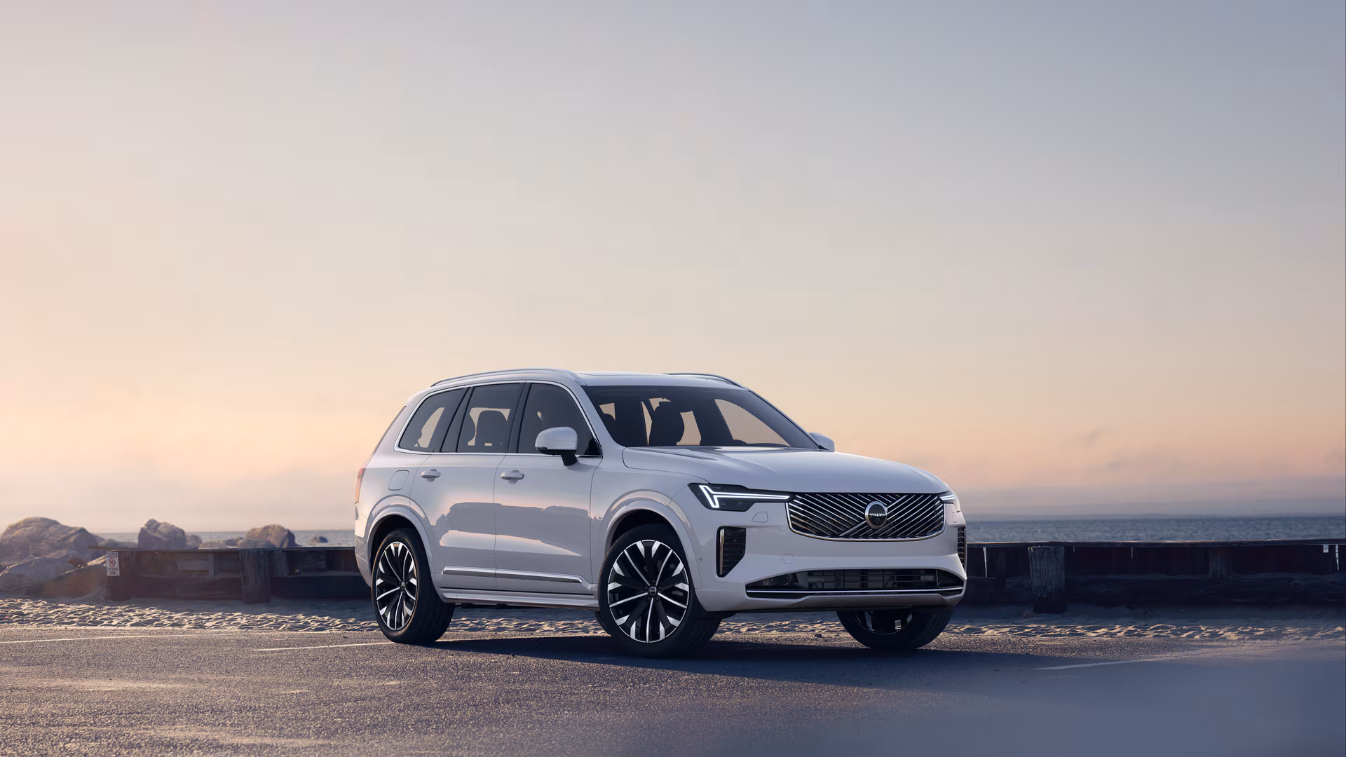 Автомобиль Volvo в три четверти на прибрежной дороге, спереди и сбоку на безмятежном фоне океана.