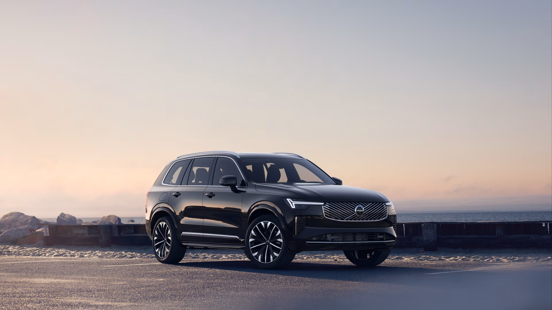 Автомобиль Volvo в три четверти на прибрежной дороге, спереди и сбоку на безмятежном фоне океана.