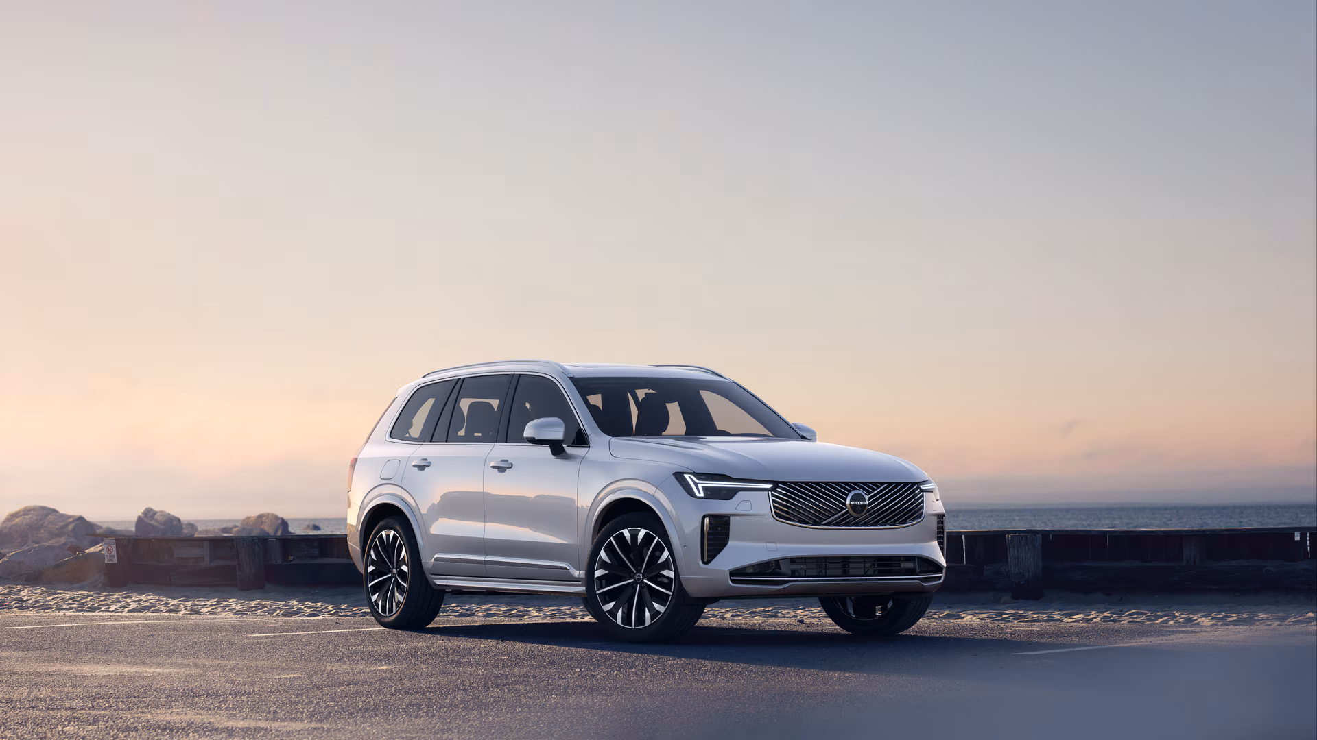 Автомобиль Volvo в три четверти на прибрежной дороге, спереди и сбоку на безмятежном фоне океана.