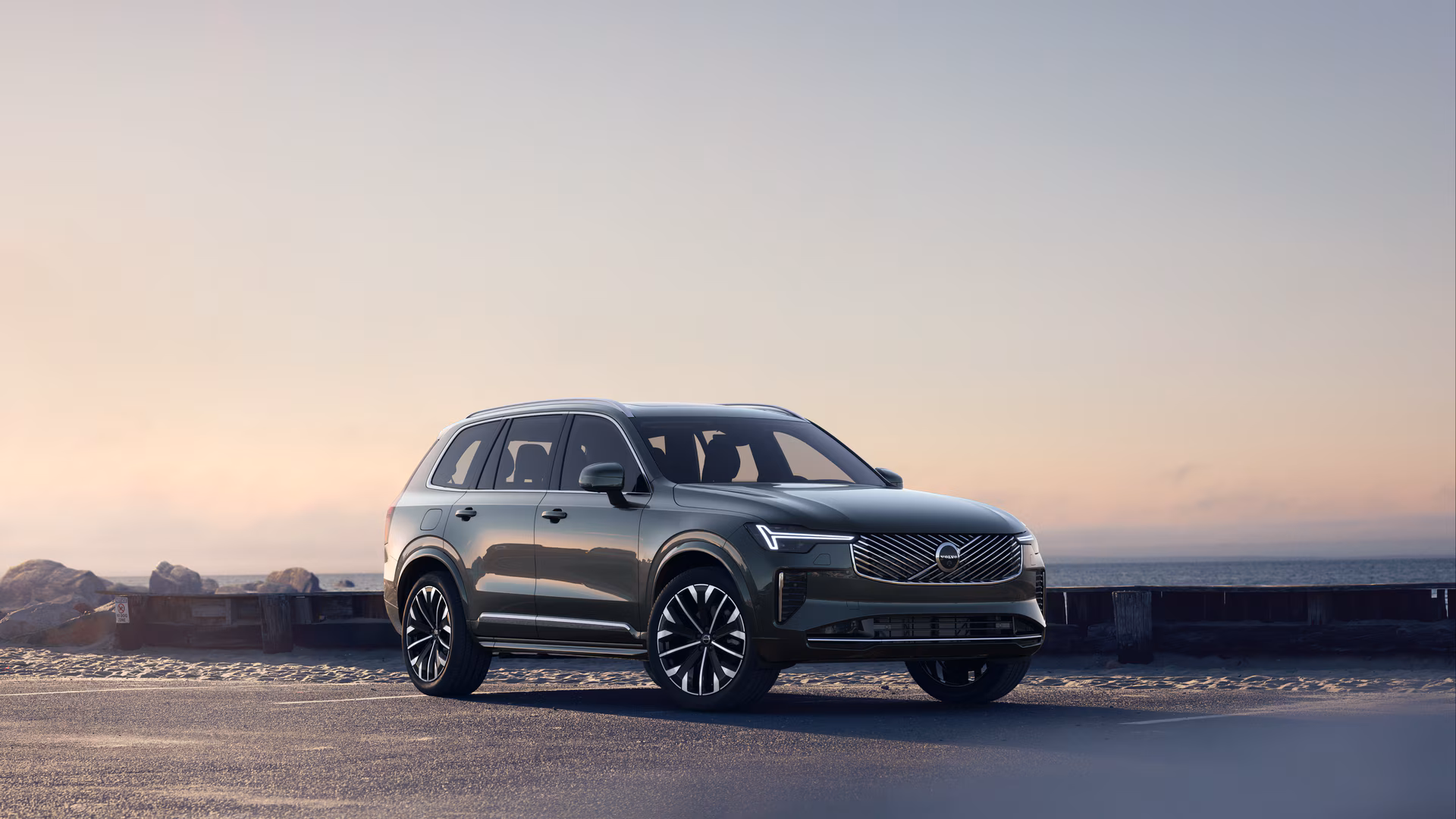 Автомобиль Volvo в три четверти на прибрежной дороге, спереди и сбоку на безмятежном фоне океана.