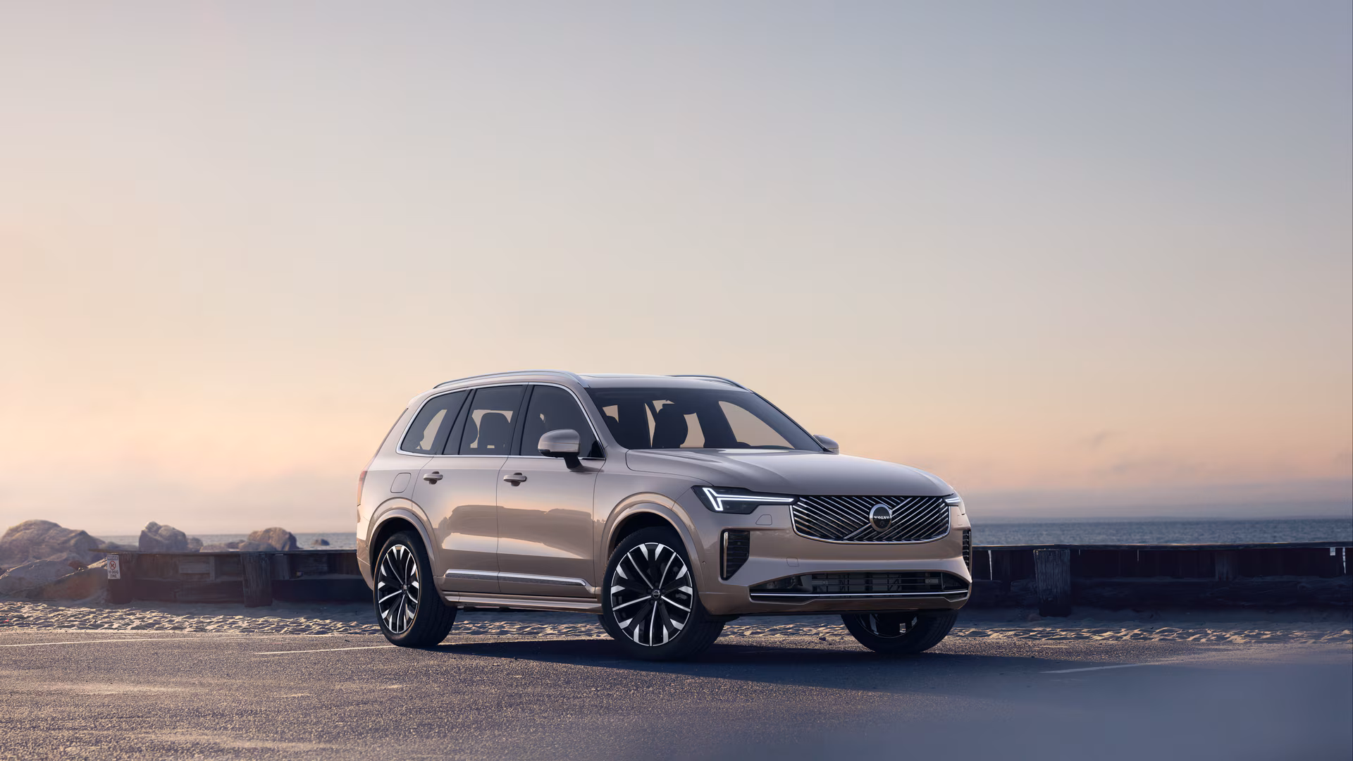 Автомобиль Volvo в три четверти на прибрежной дороге, спереди и сбоку на безмятежном фоне океана.