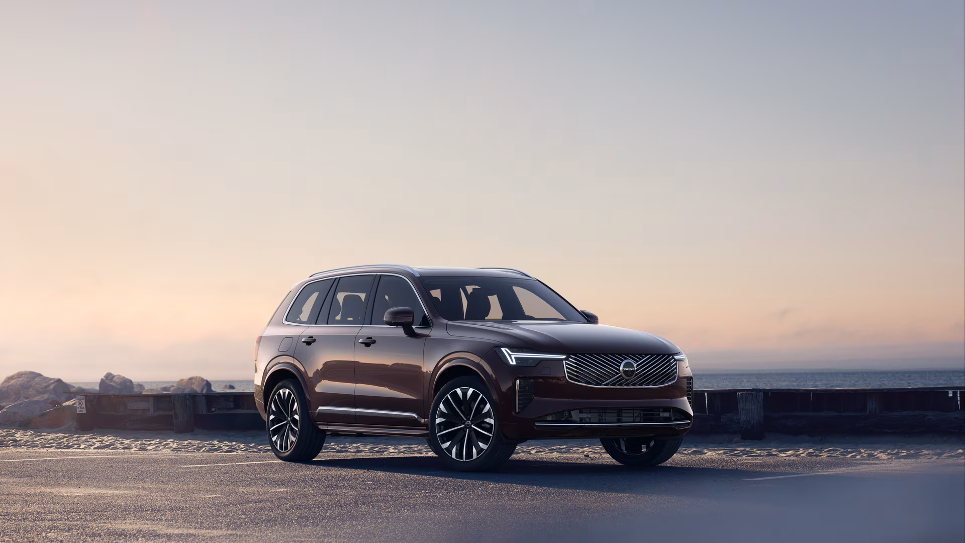 Автомобиль Volvo в три четверти на прибрежной дороге, спереди и сбоку на безмятежном фоне океана.